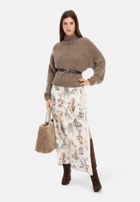 Brauner Strickpullover mit hohem Kragen, tailliert durch einen Gürtel, kombiniert mit einem bedruckten cremefarbenen Rock mit Tiermotiven. Braune Wildlederknielange Stiefel und eine flauschige Handtasche runden das Outfit ab.