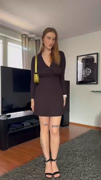 Vestido preto envolvente com mangas longas, revelando as pernas, combinado com saltos pretos com tiras. Joias prateadas, incluindo brincos, e uma pequena carteira verde.
