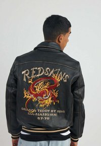 Veste en cuir noir ornée d'un grand dragon rouge brodé avec des flammes et le texte "REDSKINS" au dos. Manchons et taille côtelés.