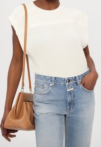 Haut en maille blanc à manches courtes, associé à un jean en denim bleu clair à taille haute. Sac à main marron texturé au design courbé, tenu à la main.