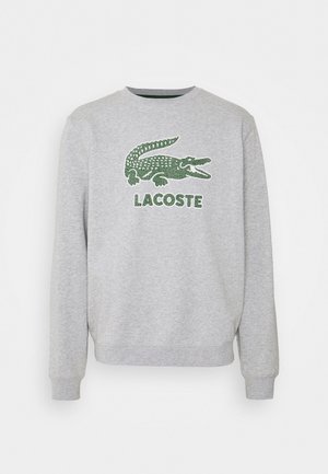 Felpa grigia con maniche lunghe, con logo coccodrillo ricamato verde e scritta "LACOSTE" sottostante. Polsini e scollo a costine.