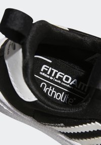 Černý textilní interiér tenisky s nápisy "FITFOAM" a "Ortholite", bílými akcenty u paty a texturovanou podrážkou.
