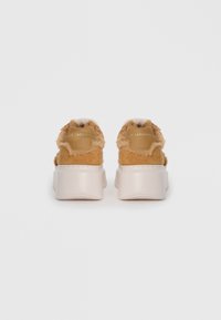 Des baskets en daim beige avec une texture moelleuse, semblable à de la fourrure, et une semelle épaisse blanche. Présente un branding subtil à l'arrière.