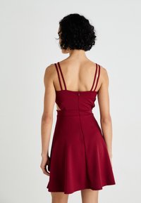Bordowa sukienka bez rękawów z dopasowanym gorsetem, wyciętymi bokami i rozkloszowanym dołem. Posiada cienkie ramiączka i ukryty zamek błyskawiczny z tyłu.