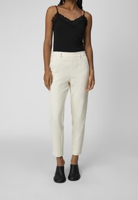 Pantalon blanc sur mesure avec une texture lisse, doté de poches latérales et d'une coupe ajustée. Associé à un débardeur noir orné de dentelle.