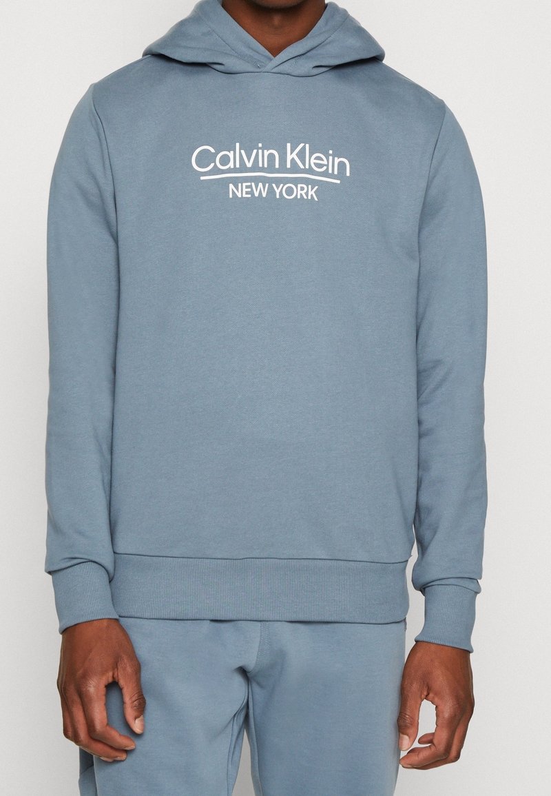 Felpa leggera azzurro chiaro realizzata in morbido misto cotone, con tasca a marsupio, polsini e orlo in costina, e logo bianco "Calvin Klein New York".