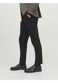 Schwarze maßgeschneiderte Hosen mit schmaler Passform, ausgestattet mit frontalen Taschen und glatter Textur, kombiniert mit glänzenden schwarzen Slippern.