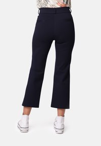 Pantalones acampanados azul marino con una textura suave, que cuentan con dos bolsillos traseros y una cintura de altura media, combinados con botas blancas hasta el tobillo.