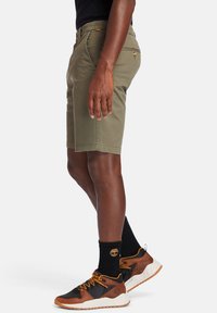 Khaki shorts med en skræddersyet pasform, lavet af letvægtsstof, med forlommer og lynlås. Kombineret med flerfarvede sneakers og sorte sokker.