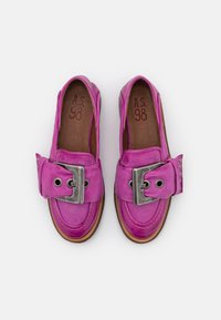 Mocassins en cuir rose avec une grande boucle argentée, des surpiqûres contrastantes et un design à bout arrondi. Semelle marron avec des accents texturés.