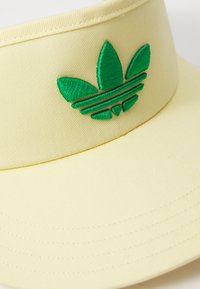 Boné amarelo com viseira e logótipo verde bordado apresentando três folhas e riscas horizontais. Tecido suave, aba curvada e detalhes costurados.