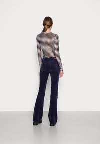 Haut en mesh à manches longues, à carreaux noir et blanc, associé à un pantalon évasé en velours côtelé bleu marine avec poches arrière et une finition texturée.