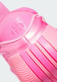 Close-up of a pink sneaker heel with textured sole and embossed logo on shiny synthetic material.