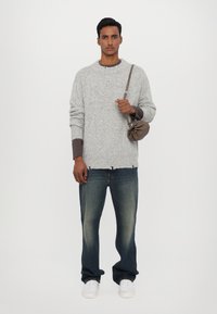 Gray knitted sweater with ribbed cuffs, paired with dark blue jeans. A small brown bag hangs from the shoulder, worn with white sneakers.