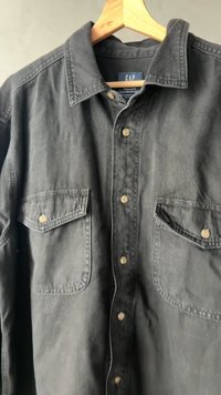 Črna denim srajca z udobnim krojem, ki ima dve sprednji žepov, gumbe za zapiranje in klasičen ovratnik. Tkanina ima mehak občutek.