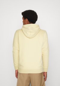 Felpa gialla con cappuccio a coulisse, polsini e orlo a costine. Tessuto morbido e design semplice senza loghi o motivi visibili.