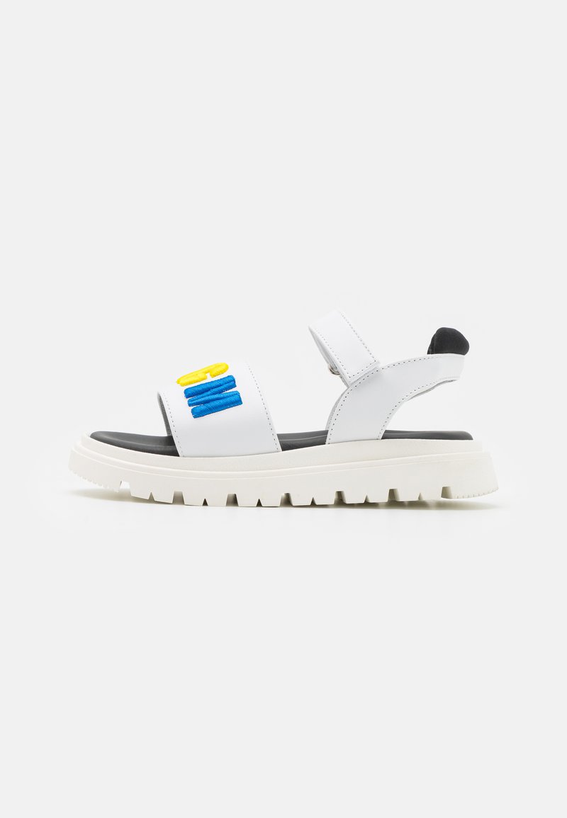 Sandales blanches avec une semelle noire texturée. Présentent deux brides ajustables, dont une avec des accents brodés jaunes et bleus.