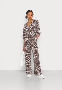 Conjunto de duas peças com padrão de zebra em marrom e branco, com um top estilo wrap e calças largas, com uma textura suave. Combinado com uma bolsa branca.