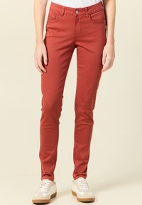 Pantaloni aderenti rossi realizzati in un misto cotone, dotati di tasche frontali, chiusura con bottone e una texture liscia. Abbinati a sneaker bianche.