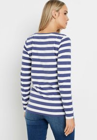 Pitkähiha, pyöreäkauluksinen paita, jossa on tummansinisiä ja valkoisia vaakaraitoja, valmistettu pehmeästä kankaasta, suoralla leikkauksella ja hieman taaksepäin kaarevalla helman kohdalla.