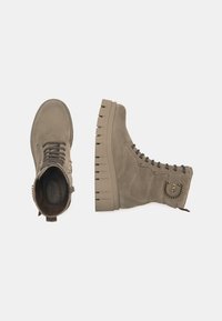 Bottines en suède beige avec une surface texturée, fermeture à lacets et une semelle épaisse à plateforme avec des détails dénotés. Accent en chaîne métallique sur le côté.