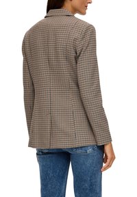 Brauner Blazer mit Karomuster und taillierter Passform, ausgestattet mit einem Reverskragen und transparenter Struktur, kombiniert mit blauen Jeans.