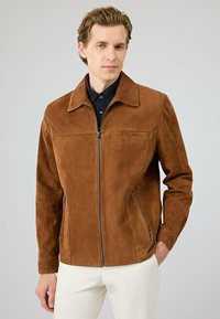 Bruine suedew jacket met een puntige kraag, rits aan de voorkant, zijzakken en een gladde textuur. Draagt over een zwart poloshirt.