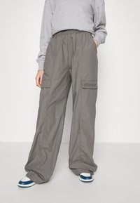 Šedé cargo kalhoty s širokým, volným střihem, obsahující boční kapsy a elastický pas na šňůrku, doplněné modro-bílými teniskami.