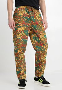 Färgglada, löst sittande byxor med en brun bas och mönster av gröna, gula och röda prickar. Inkluderar en elastisk midja med snörning.