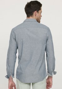 Chemise bleu clair à manches longues en tissu texturé. Présente un col classique, des poignets à boutons et un ourlet arrondi, vue de dos.
