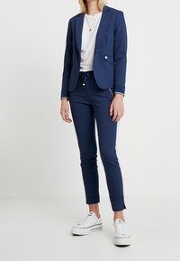 Mörkblå kavaj med skräddarsydd design, enkel knapp och subtila vita sömmar, tillsammans med matchande slim-fit byxor med sidostråk.