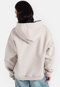 Jasno beżowy oversize'owy hoodie z kapturem na sznurku, ściągaczami na rękawach i teksturowanym wykończeniem, połączony z jasnoniebieskimi dżinsami.