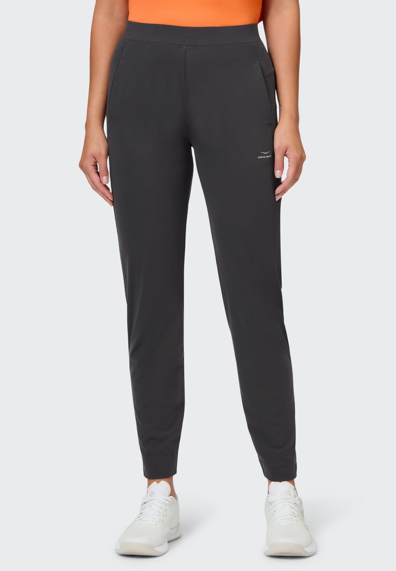 Dunkelgraue Jogginghosen mit einer glatten Textur, ausgestattet mit seitlichen Taschen und einer figurschmeichelnden Passform, kombiniert mit weißen Sportschuhen.