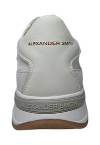 Weiße Sneaker mit einer strukturierten grauen Ferse, geprägtem Markennamen in Braun und einer Gummisohle mit einem kontrastierenden hellbraunen Boden.