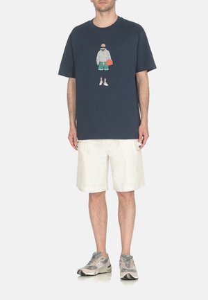 Camiseta de manga corta azul marino con un estampado gráfico de una figura sosteniendo un balón de baloncesto, combinada con pantalones cortos blancos y zapatillas deportivas grises.