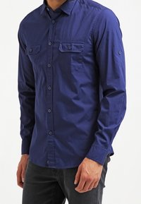 Mörkblå långärmad skjorta i bomull med knappad krage, två bröstfickor och knäppte ärmslut.