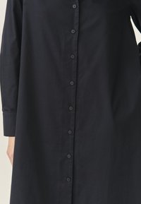 Tumedast sinisest puuvillast nööpideta särk, millel on pikad varrukad, lõdva istuvuse ja nähtavad nupud ees. Siledat tekstuuri kogu särk.