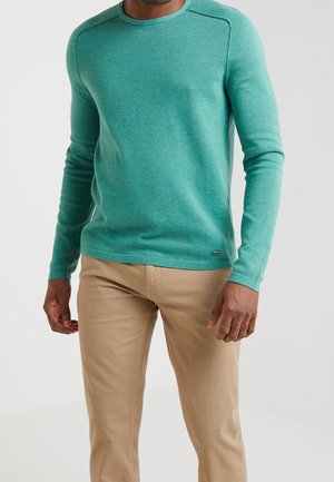 Turquoise lange mouwen trui met een ronde hals, gemaakt van een gestructureerd materiaal, gecombineerd met lichtbeige broeken. Kenmerkt zich door naaddetails op de schouders.