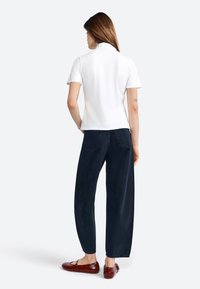 Weißes kurzärmeliges Poloshirt kombiniert mit dunkelblauen weit geschnittenen Jeans und braunen flachen Schuhen, mit einer glatten Materialoberfläche und einem lässigen Design.