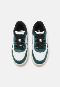Sneaker bianchi con dettagli teal scuro, lacci neri e suola in gomma, dotati di un colletto e una linguetta imbottiti per il comfort.