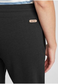 Zwarte katoenen joggers met een geribde tailleband, zijzakken en een klein, opgedrukt logo-label in een lichte kleur. Zachte textuur zichtbaar.