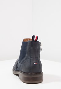 Kožená námořnická kotníková bota s elastickými bočními panely, strukturovaným povrchem, kulatou špičkou a hnědým dřevěným podpatkem. Obsahuje značkovou poutko pro snadné nazouvání.