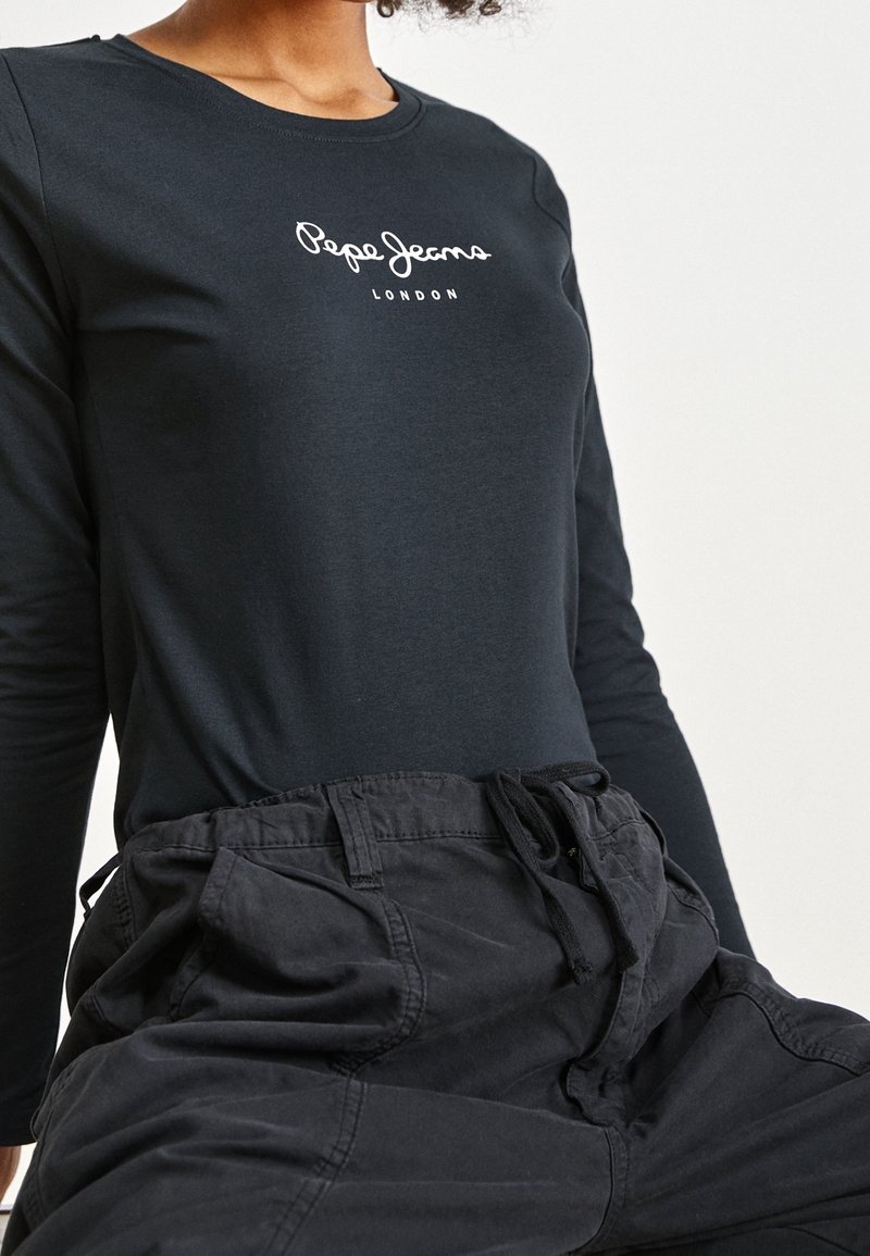 Černé tričko s dlouhým rukávem a kulatým výstřihem, na hrudi s bílým logem "Pepe Jeans London", v kombinaci s volnými černými kalhotami.