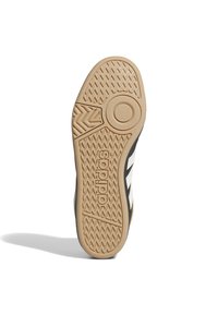 Adidas sneakersula med ett texturerat mönster i beige gummi och en cirkulär accent, kompletterad med svart och vita ränder på ovandelen.