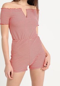 Röd och vit randig off-shoulder romper med korta ärmar, V-ringning, elastisk midja och åtsittande short. Slät tyg med diskret volangdetalj.
