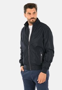 Giacca bomber blu navy con zip frontale, polsini e colletto a coste. Presenta tasche laterali e un tessuto morbido e leggero per il comfort.