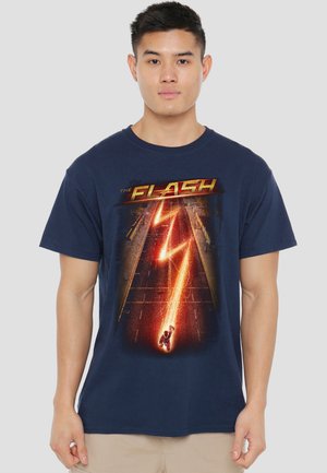 Young man wearing navy blue T-shirt with lightning bolt and "The Flash" text over a city street background.