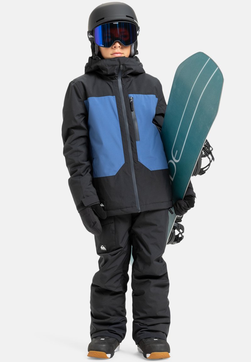 Czarna i niebieska kurtka snowboardowa z zamkiem błyskawicznym, czarne spodnie, rękawice i zielona deska snowboardowa. W komplecie czarny kask i gogle.