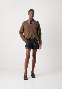 Brun strikket v-hals sweater, faux læder sorte shorts med bælte og sorte hæle sandaler. Har et sort tørklæde bundet om halsen.
