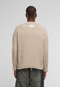 Helle beige Strickjacke mit gerippten Bündchen und Saum. Verfügt über ein Etikett am Kragen. Wird mit dunkelgrauen, weiten Jeans getragen.